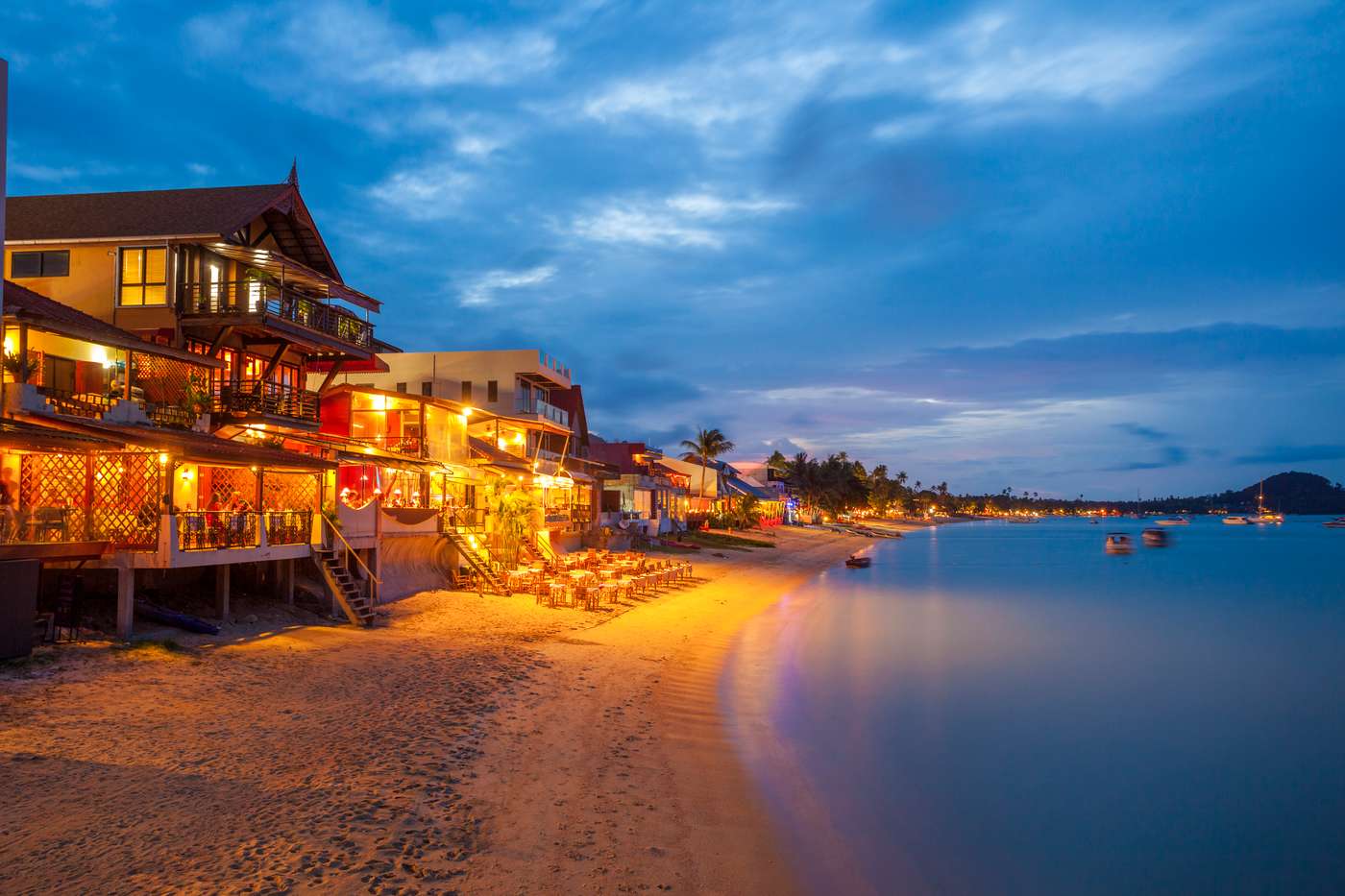 "Surat Thani, Thailand - September 28, 2011: Night time view of buildings along the beach at Bo Phut on the island of Koh Samui in Thailand. People can be seen sitting at some beachside bars."