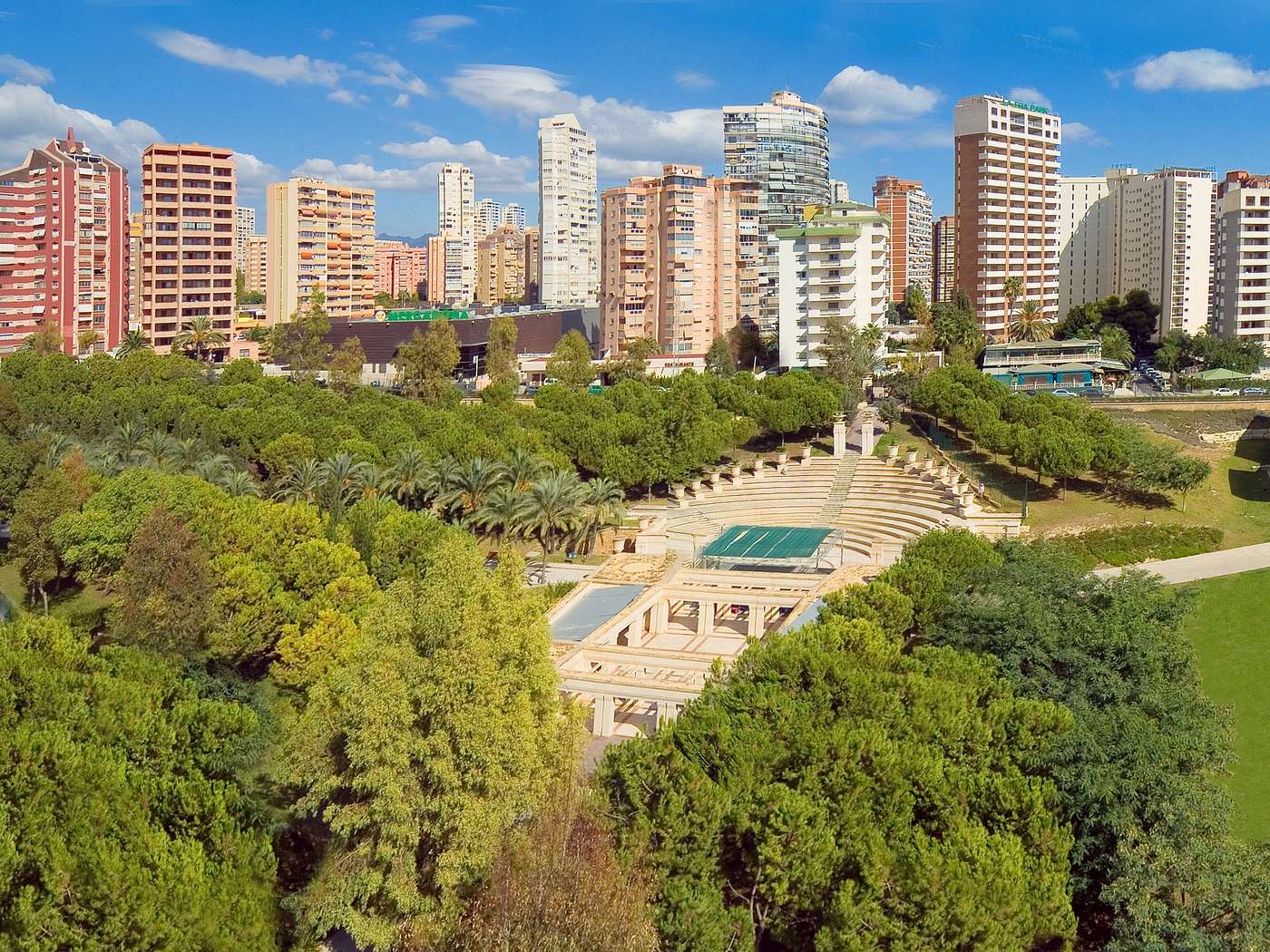 Exterior shot of surrounding gardens, trees and high-rise buildings.