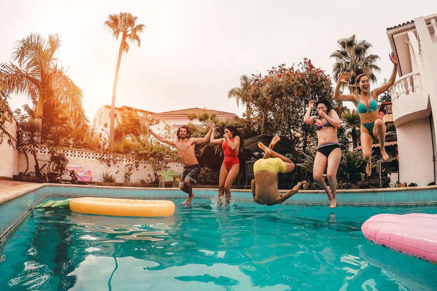 Group of happy friends jumping in pool at sunset time - Crazy young people having fun making party in exclusive tropical house - Holidays, summer, vacation and youth lifestyle concept