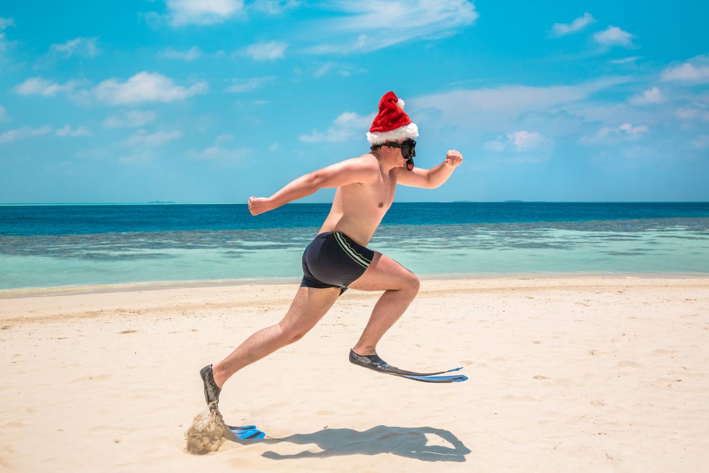 Man running across beach in Santa hat, flippers and snorkel