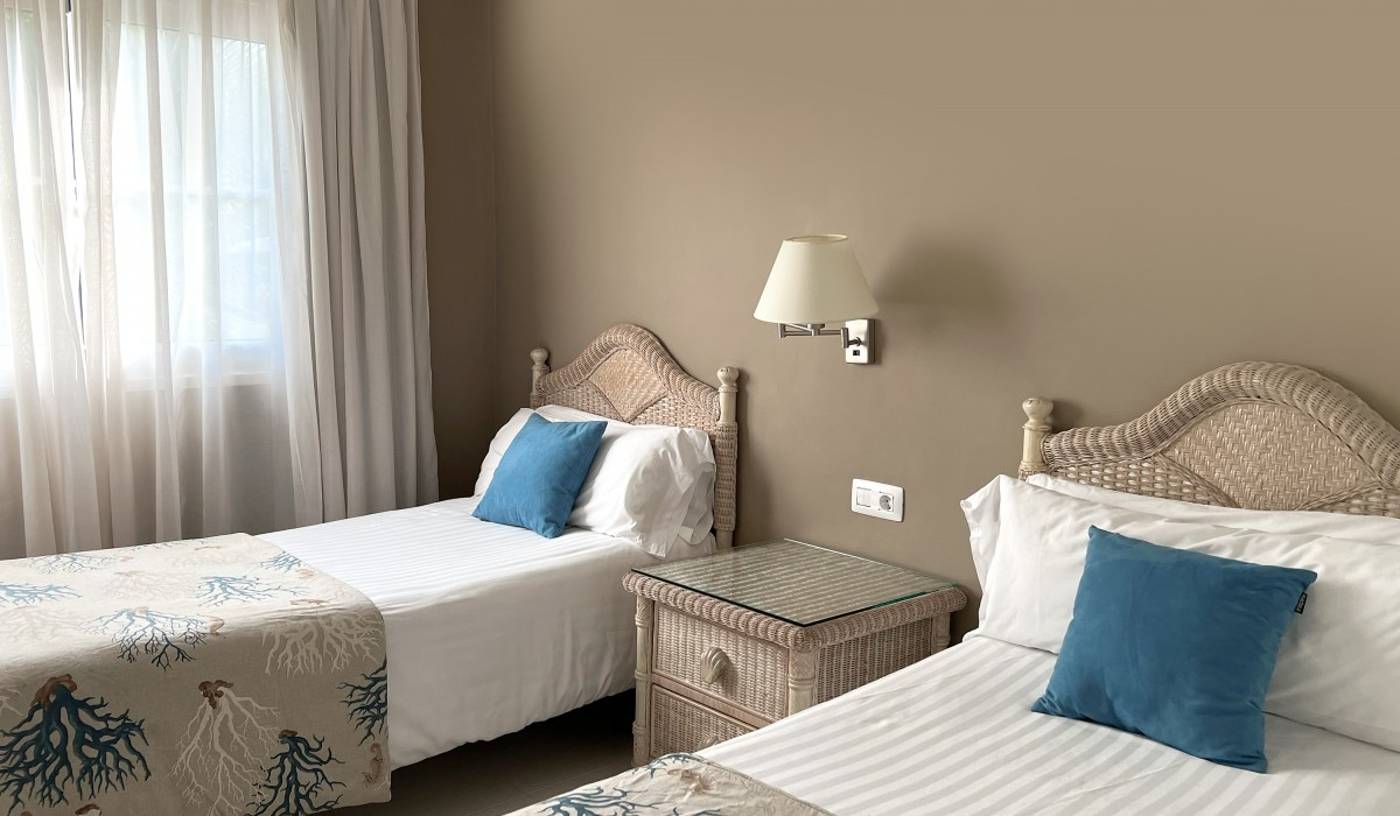 Twin beds and one bedside table in the middle. Stylish tulle curtains.