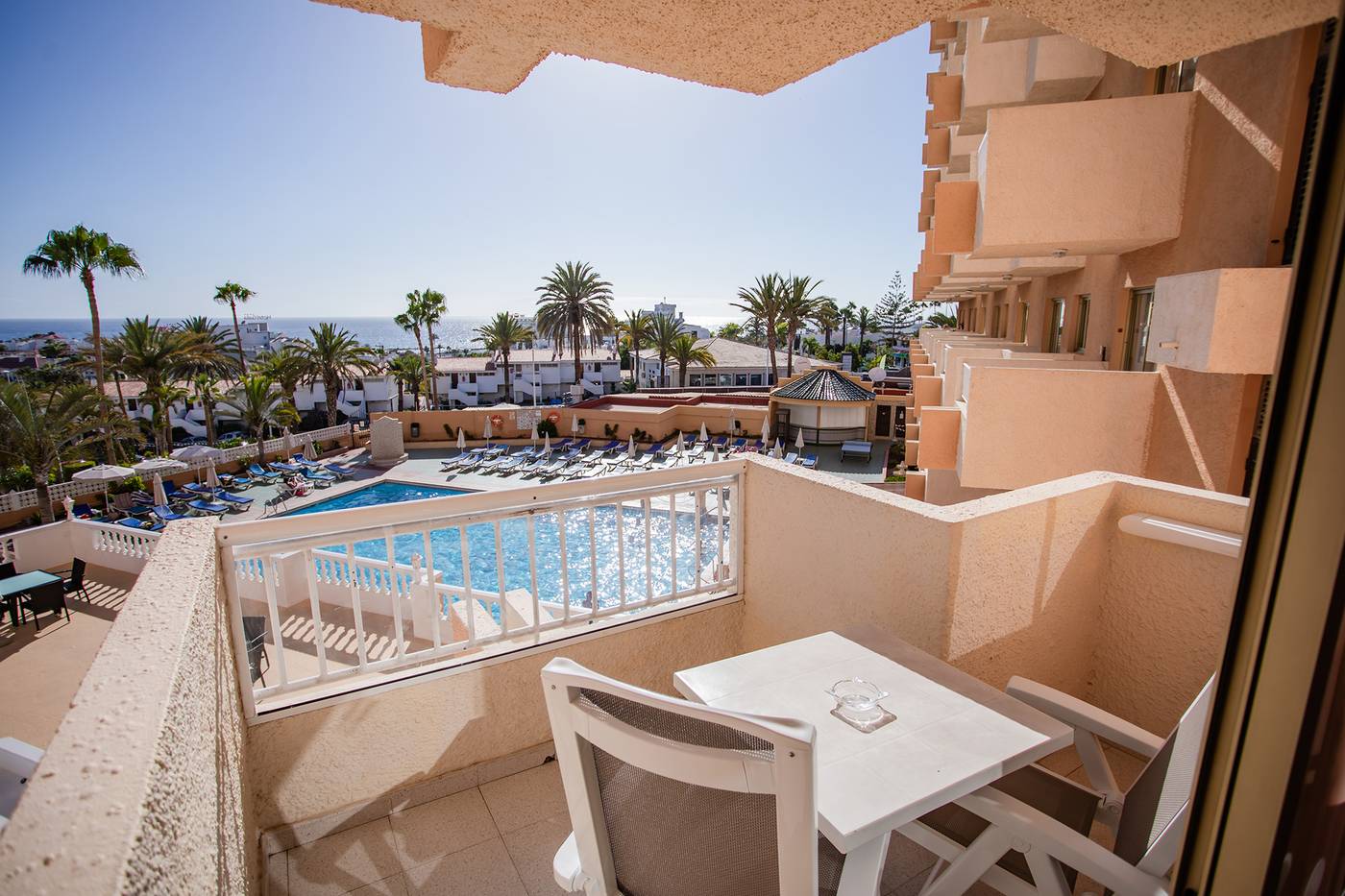 Premium One Bedroom Apartment Pool View. Balcony, furnished with table and chairs, overlooking the pool.