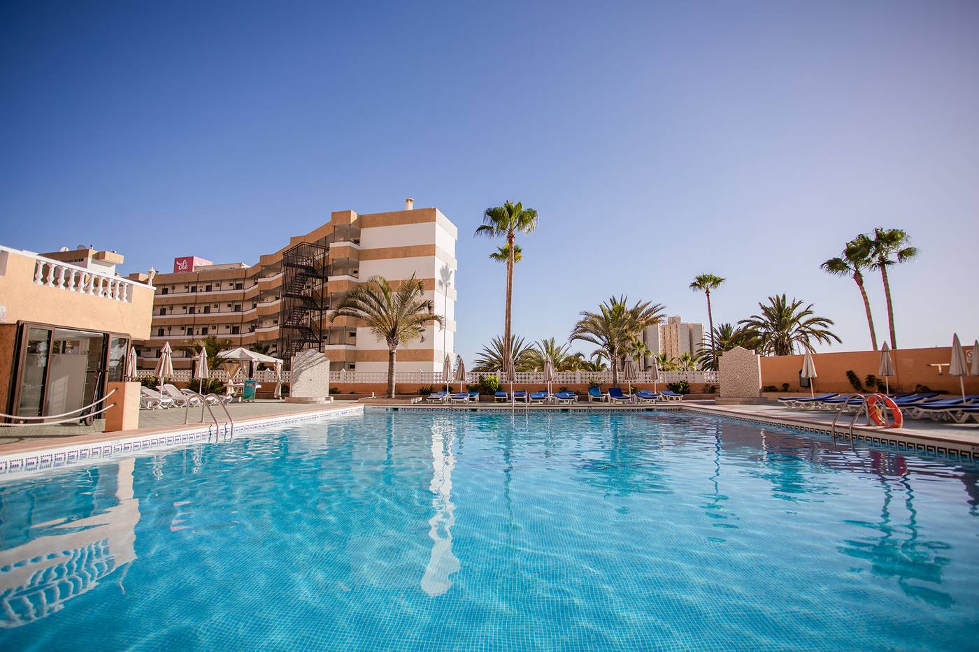 Outdoor pool with sunbeds and hotel in the background.