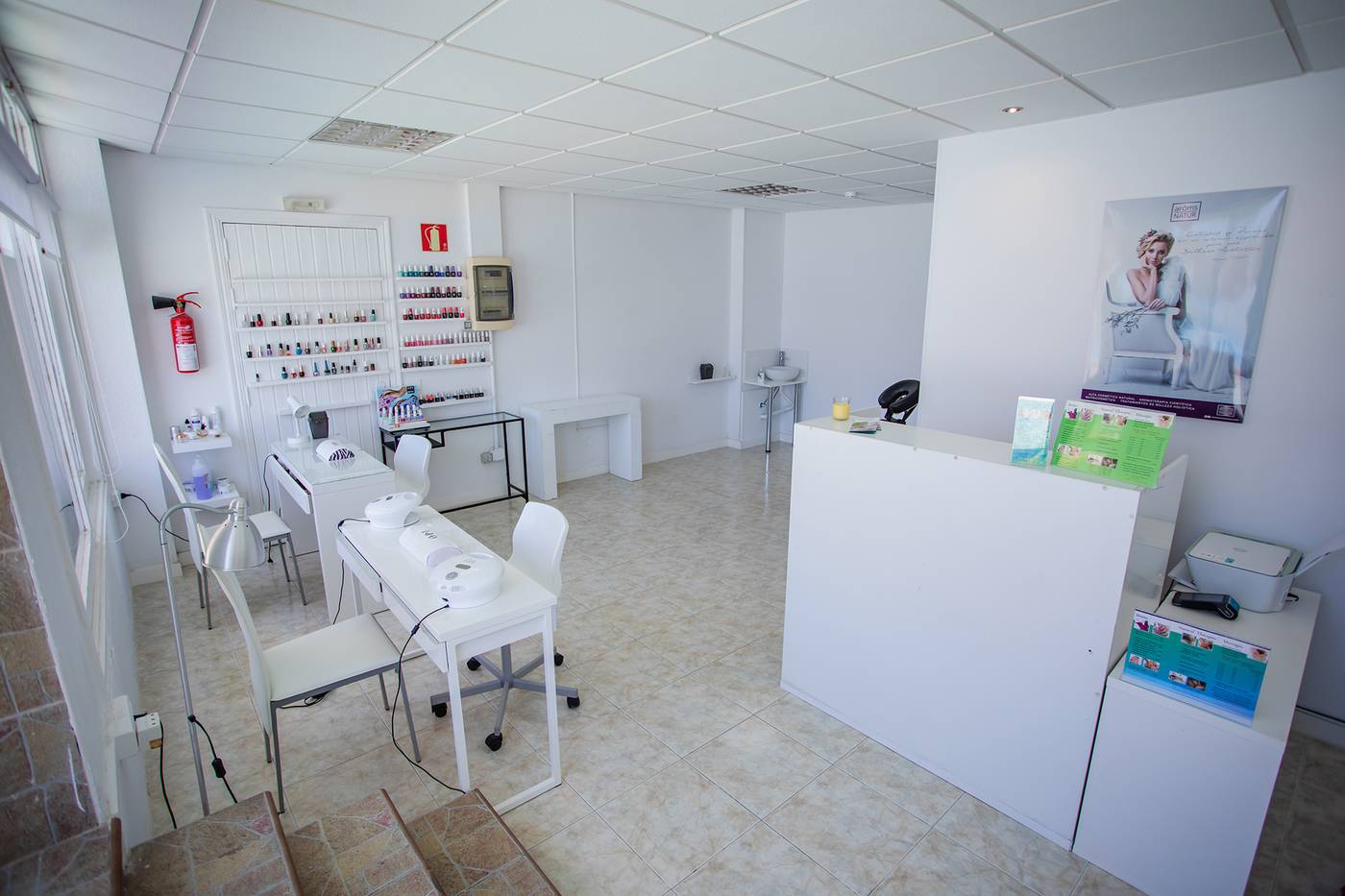 Nail salon, with tables and chairs and different nail polishes on shelves.