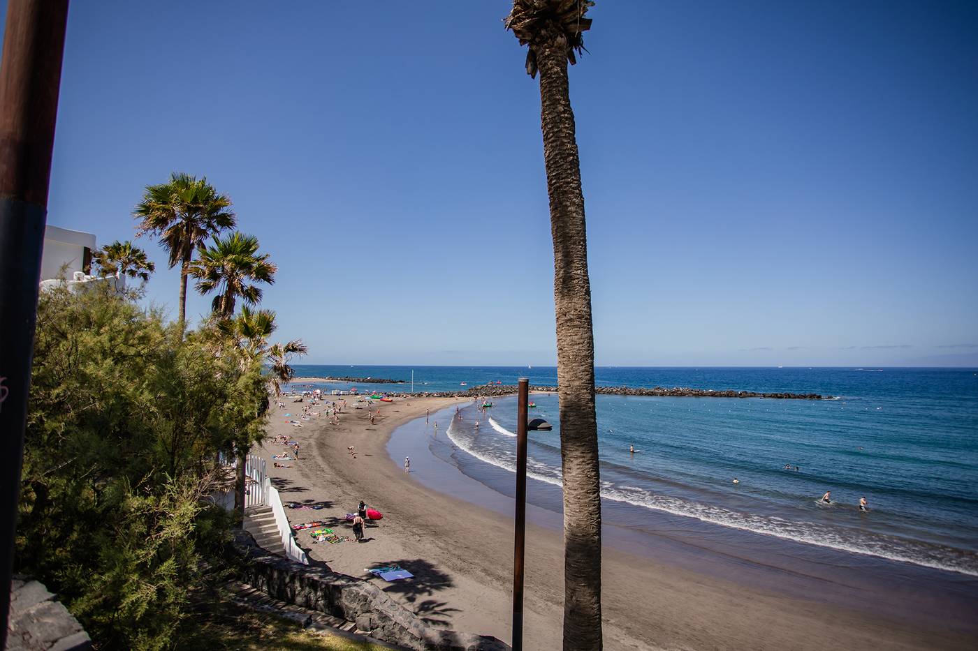 Beach with waves on the shore, wrapping round the coast. Lined with palm trees.