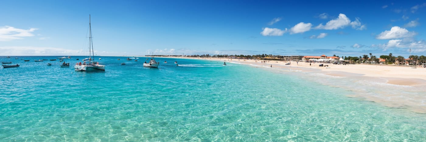 Boats floating by the white-sand shore on a beautifully clear sea.